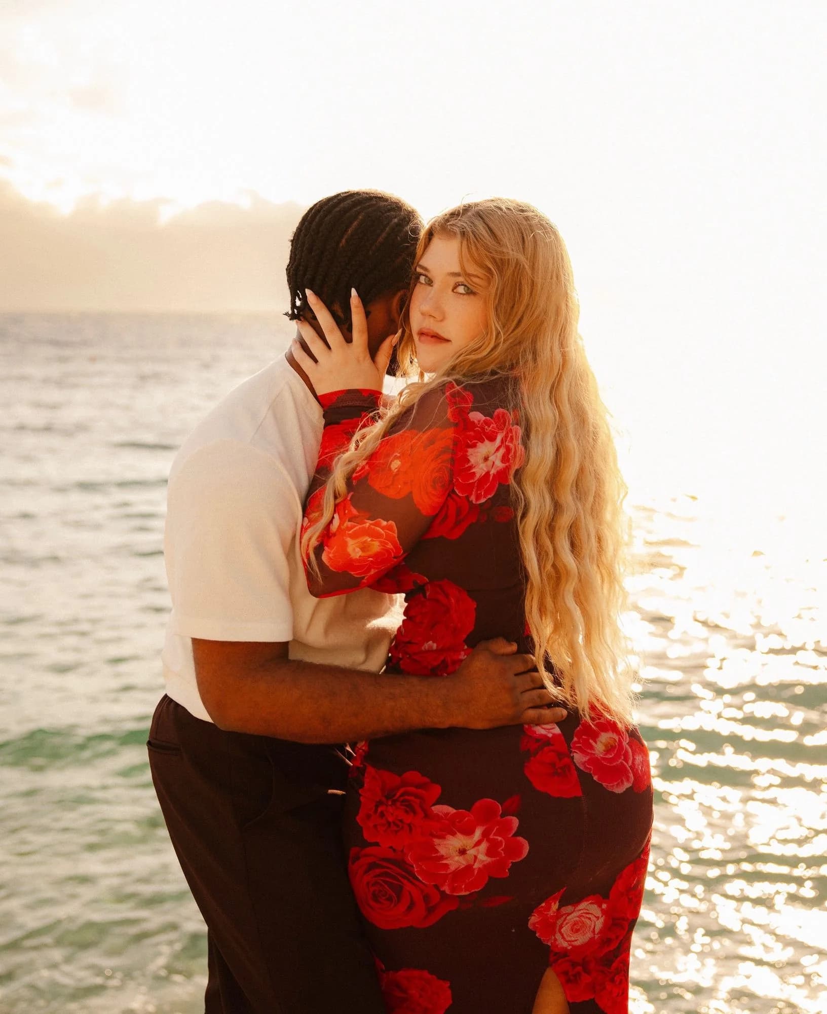 Alicia and Ese holding each other by the sea at sunset, Alicia looking back over her shoulder